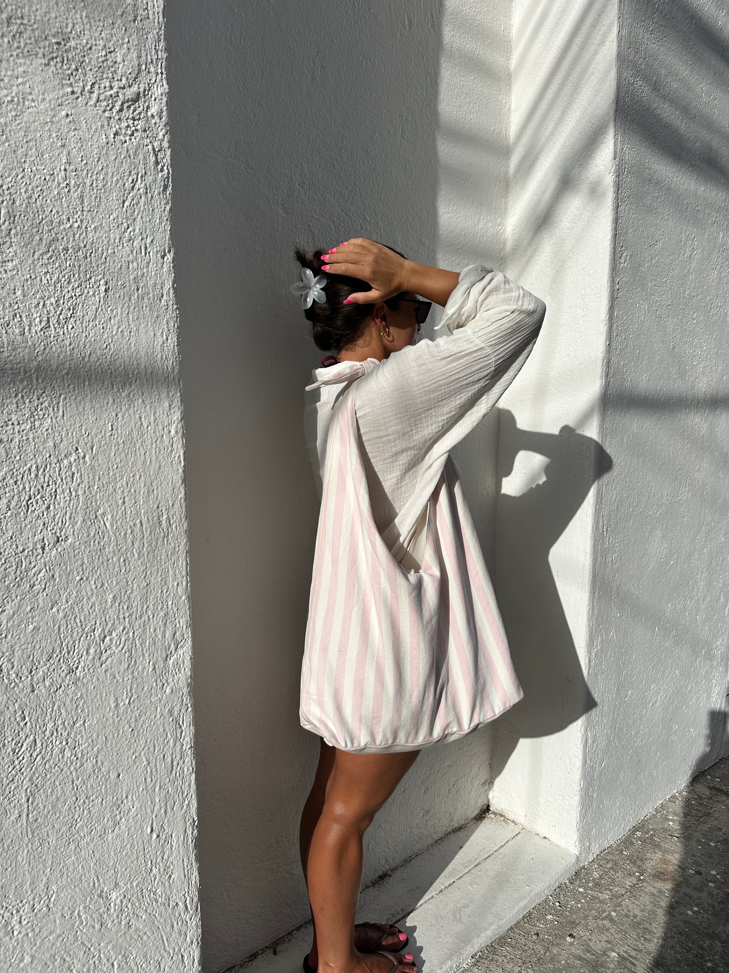 Person standing beside a a concrete  building surface with a pink and white striped tote bag