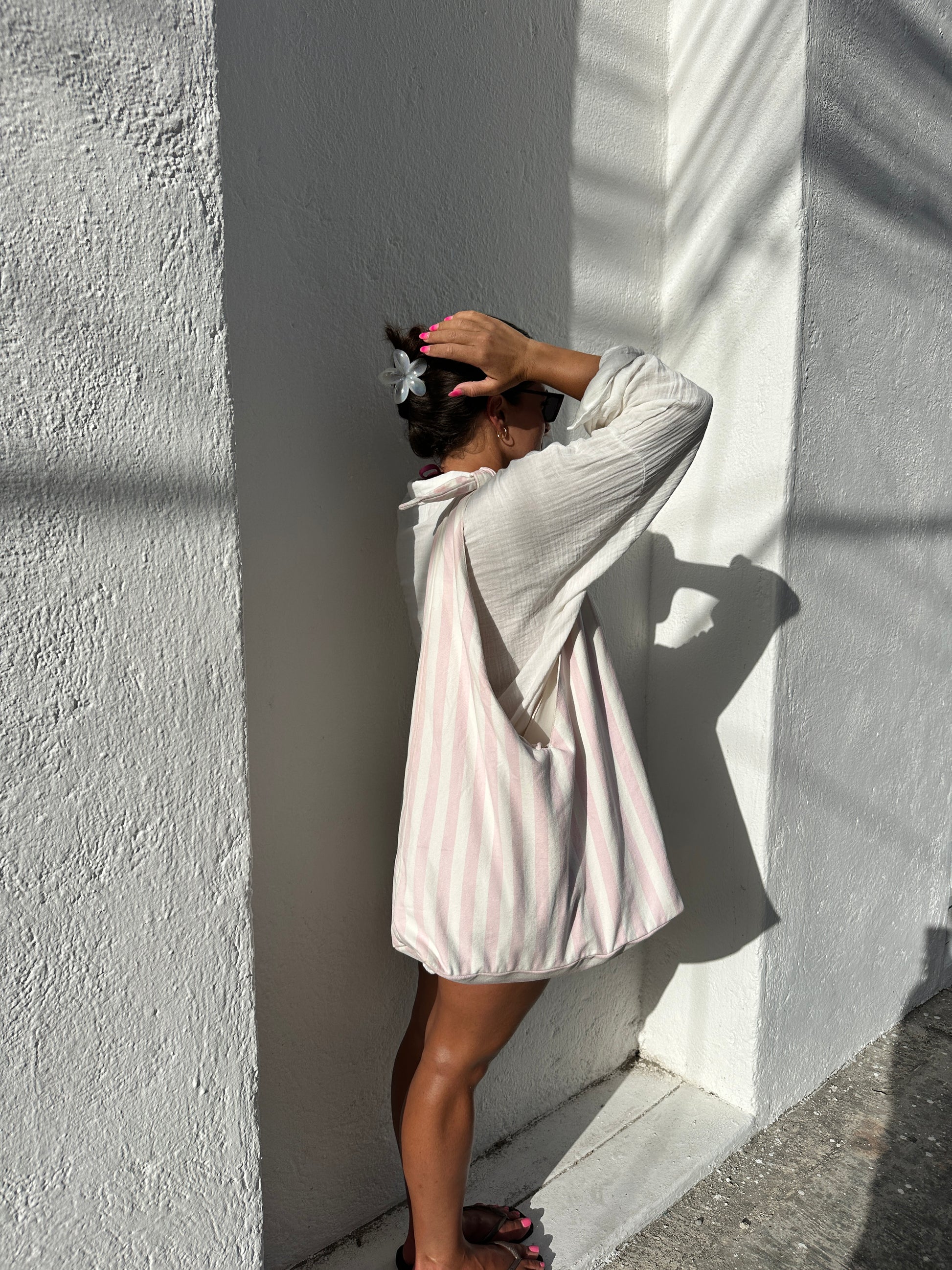 Person standing beside a a concrete  building surface with a pink and white striped tote bag