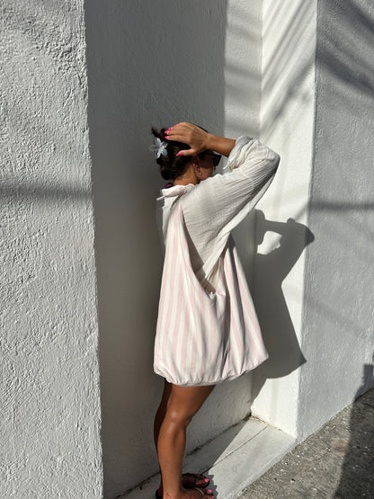 Person standing beside a a concrete  building surface with a pink and white striped tote bag